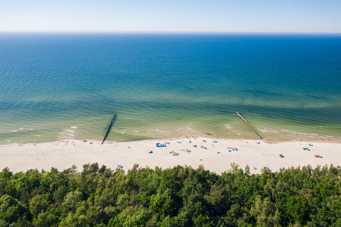 Luchtfoto van een rustige zandstrand met weinig mensen, blauwe zee en bos bij 'Ustecka Osada 45m2'.