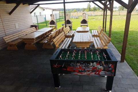 Overdekte buitenruimte bij Domki wakacyjne Przewłoka met houten tafels, banken, kicker en barbecuetoestellen.