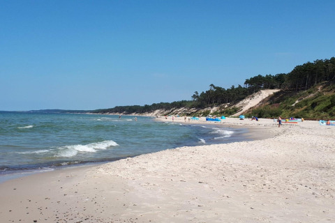 Zandstrand met zachte golven, beboste duinen en enkele mensen bij Domki wakacyjne Przewłoka in Denemarken.