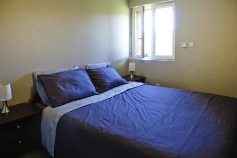 Slaapkamer met dubbel bed, donkerblauw beddengoed, nachtkastjes en een open raam bij Holiday home «Le Porge», Frankrijk.