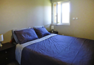 Dormitorio con cama doble, ropa de cama azul oscuro, mesillas y ventana abierta en Holiday home «Le Porge», Francia.