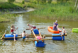 Kinderen spelen op een vlot en kano op het water bij Minicamping Falkenborg in Gelderland, Nederland.