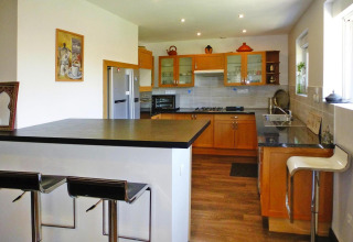 Cocina moderna con gabinetes de madera, taburetes y ventanas grandes en Holiday home «Le Porge», Francia.