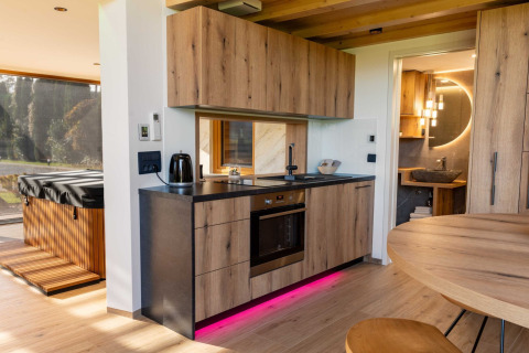 Modern lodge kitchen with wooden cabinets, pink LED lighting, view of hot tub, and door to bathroom.
