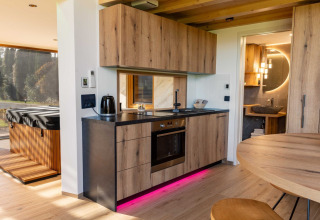 Modern lodge kitchen with wooden cabinets, pink LED lighting, view of hot tub, and door to bathroom.