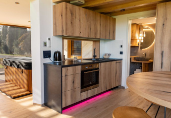 Cuisine moderne en bois dans un lodge avec éclairage LED rose, vue sur jacuzzi et porte vers la salle de bain.