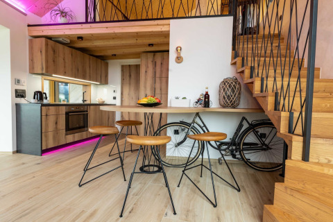 Modern lodge interior with wooden kitchen, bar stools, and bicycle storage under staircase.
