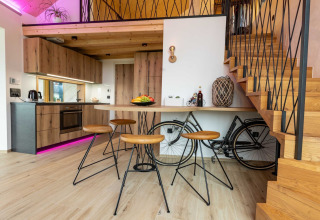 Modern lodge interior with wooden kitchen, bar stools, and bicycle storage under staircase.