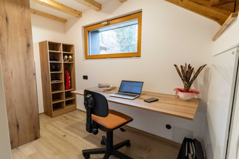 Modern lodge office with wooden desk, laptop, shelving, and potted plant, photographed in Slovenia.