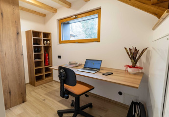 Ufficio moderno in lodge con scrivania in legno, laptop, scaffale e pianta, fotografato in Slovenia.