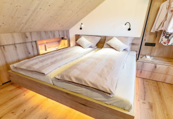 Camera da letto moderna e accogliente in lodge sloveno con letto matrimoniale, legno e luci soffuse.