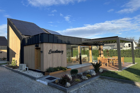 Modern lodge in Slovenia with solar panels, wooden exterior, and a sunny patio with outdoor furniture.