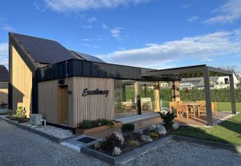 Moderne lodge in Slovenië met zonnepanelen, houten gevel en zonnig terras met tuinmeubilair.
