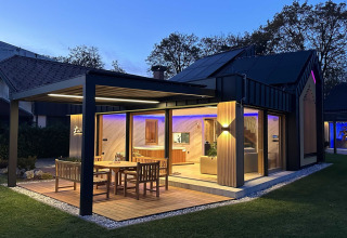 Modern Slovenian lodge with illuminated patio, outdoor dining set, large windows and cozy interior at dusk.