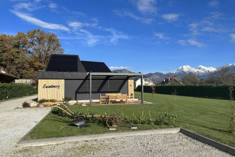 Modern Excellency lodge with solar panels, lawn, and mountain views in Slovenia under a clear blue sky.