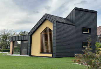 Modernes Ferienhaus mit schwarzer Fassade, großem Fenster und gepflegtem Rasen, gelegen in Slowenien.