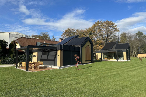 Modern holiday lodge with black roof, large windows, green lawn, and outdoor dining area in Slovenia.