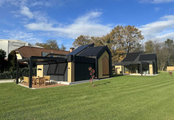 Lodge per vacanze moderno con tetto nero, grandi finestre e prato verde in Slovenia.