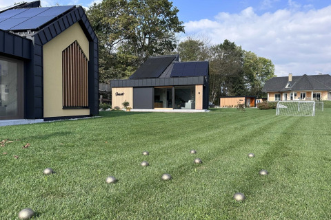 Modern lodge in Slovenia with large glass windows, green lawn, small metallic balls scattered on grass.