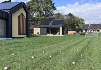 Lodge moderno in Slovenia con ampie vetrate, prato verde e piccole sfere argentate sparse sull’erba.