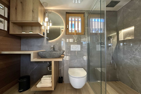 Modern bathroom with rain shower, vessel sink, wood accents, and round mirror at a lodge in Slovenia.