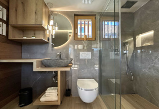 Modern bathroom with rain shower, vessel sink, wood accents, and round mirror at a lodge in Slovenia.