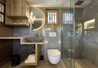 Baño moderno con ducha tipo lluvia, lavabo de piedra y detalles en madera en lodge de Eslovenia.