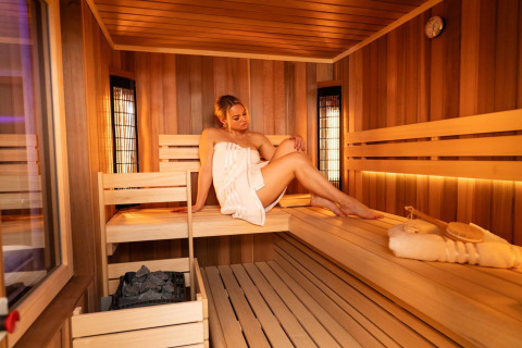 Woman relaxing in sauna at Elegant Warm Bliss Hideaway Escape Lodge in Slovenia, wrapped in towel.