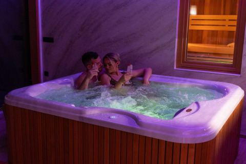 A couple relaxes in a hot tub with drinks at Elegant Warm Bliss Hideaway Escape Lodge, Slovenia.