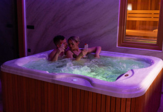 A couple relaxes in a hot tub with drinks at Elegant Warm Bliss Hideaway Escape Lodge, Slovenia.