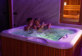 Een koppel ontspant in een jacuzzi met drankjes bij Elegant Warm Bliss Hideaway Escape Lodge, Slovenië.
