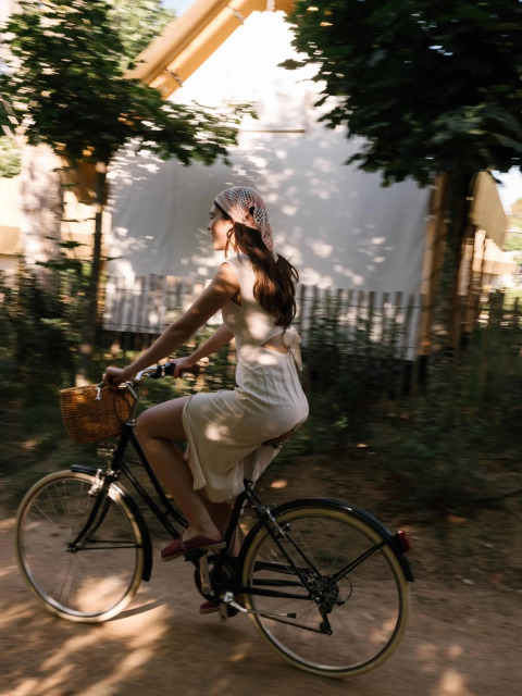 Donna con abito estivo in bicicletta con cestino al parco vacanze Wecamp Santa Cristina in Catalogna.