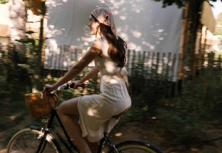 Woman in a summer dress rides a bike with a basket at Wecamp Santa Cristina holiday park in Catalonia.