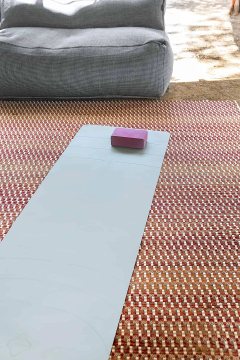 Yogamat met paarse blok op een patroonkleed voor een grijze zitzak bij Wecamp Santa Cristina, Spanje.