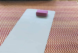 Yogamatte mit lila Block auf gemustertem Teppich vor grauem Sitzsack im Wecamp Santa Cristina Park.