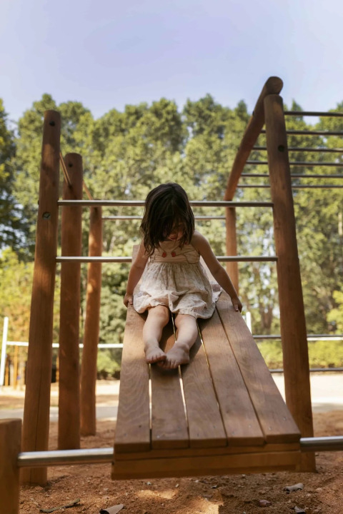 Una bambina gioca su uno scivolo di legno al Wecamp Santa Cristina, Catalogna, Spagna, tra gli alberi.
