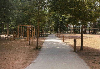 Weg durch einen baumbestandenen Bereich mit Holz-Fitnessgeräten im Wecamp Santa Cristina, Katalonien.