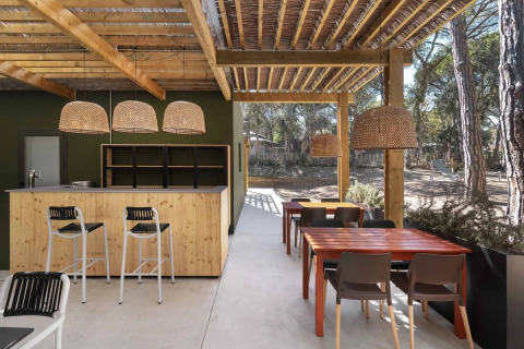 Outdoor seating area at Wecamp Santa Cristina, Catalonia, featuring wooden tables, bar, and wicker lights.