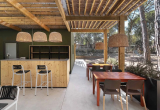Buitenruimte van Wecamp Santa Cristina in Catalonië met houten tafels, bar en rieten lampen.