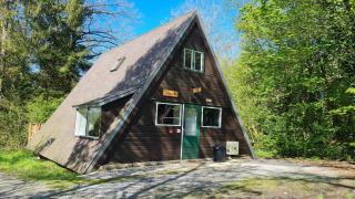 A-förmiges Holzhaus namens Chalet Nr. 186 im Grünen, umgeben von Bäumen bei sonnigem Himmel.