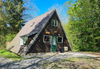 A-förmiges Holzhaus namens Chalet Nr. 186 im Grünen, umgeben von Bäumen bei sonnigem Himmel.