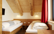 Camera accogliente nello Chalet 'Faltri' in Austria con due letti singoli, soffitto in legno e tende rosse.