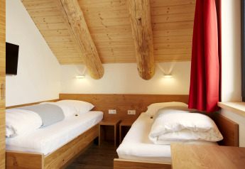 Camera accogliente nello Chalet 'Faltri' in Austria con due letti singoli, soffitto in legno e tende rosse.
