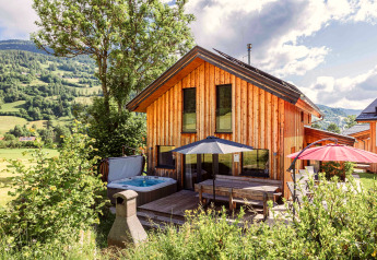 Chalet en bois avec jacuzzi extérieur, terrasse et parasols, au cœur d’un paysage alpin autrichien.
