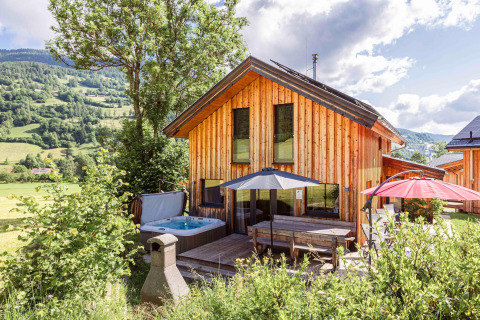 Holzchalet mit Terrasse, Sonnenschirmen und Whirlpool, umgeben von Bergen in Österreich.