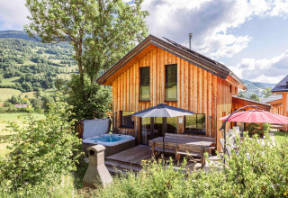 Holzchalet mit Terrasse, Sonnenschirmen und Whirlpool, umgeben von Bergen in Österreich.
