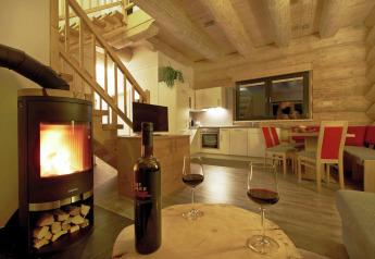 Soggiorno accogliente dello chalet «Faltri» in Austria, con stufa a legna e due bicchieri di vino rosso.