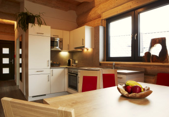 Cucina moderna nello Chalet Faltri in Austria, con mobili bianchi, grandi finestre e ciotola di frutta.
