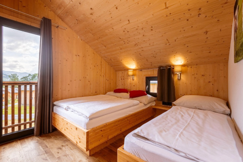 Schlafzimmer im Kreischberg Chalets 29 in Österreich mit Holzwänden, drei Betten und Balkonblick.