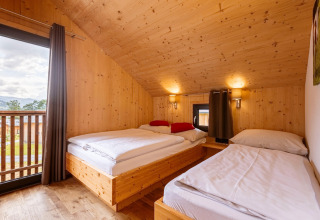 Schlafzimmer im Kreischberg Chalets 29 in Österreich mit Holzwänden, drei Betten und Balkonblick.